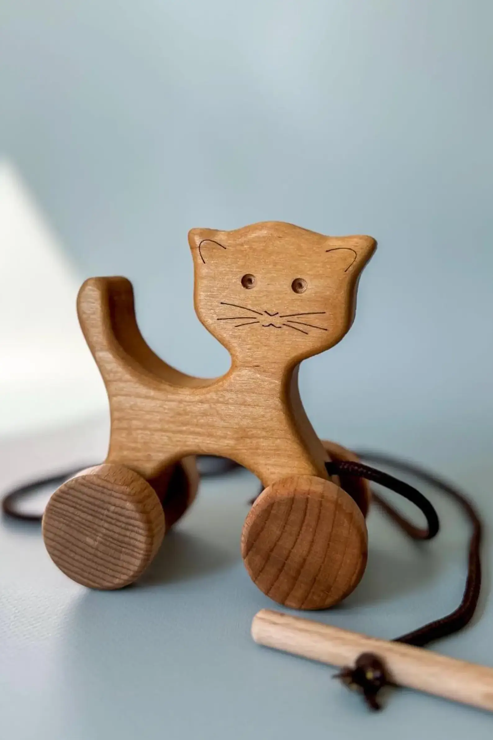 A wooden cat pull toy with brown string and a wooden handle. The cat is light brown and has a carved face with black eyes and whiskers. DKwoodentoysUA 